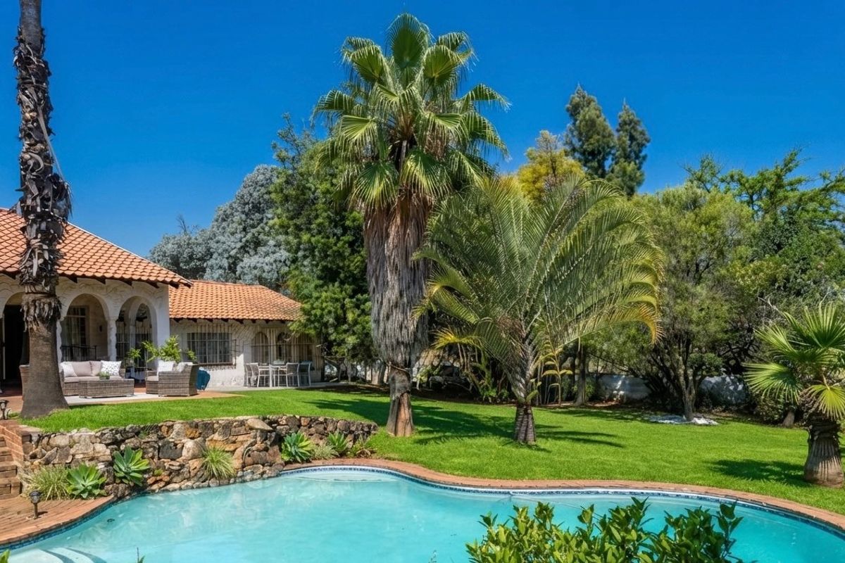 A well-maintained rear garden featuring a swimming pool, stone retaining wall, and a covered patio area with classic arched architectural details.