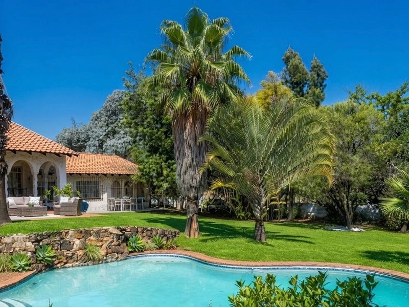 A well-maintained rear garden featuring a swimming pool, stone retaining wall, and a covered patio area with classic arched architectural details.