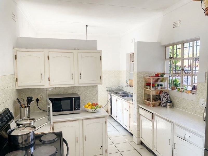 A functional kitchen featuring white built-in cabinetry, tiled backsplash, double basin sink, and electric stove, offering a classic layout with potential for modernization.
