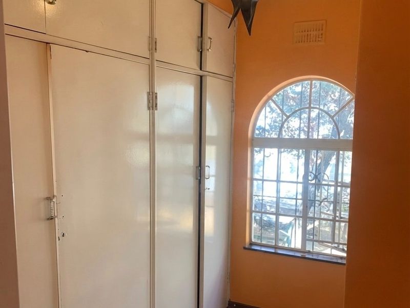 A hallway featuring extensive built-in storage cabinetry and an arched window with security bars, providing natural light and functional storage space.