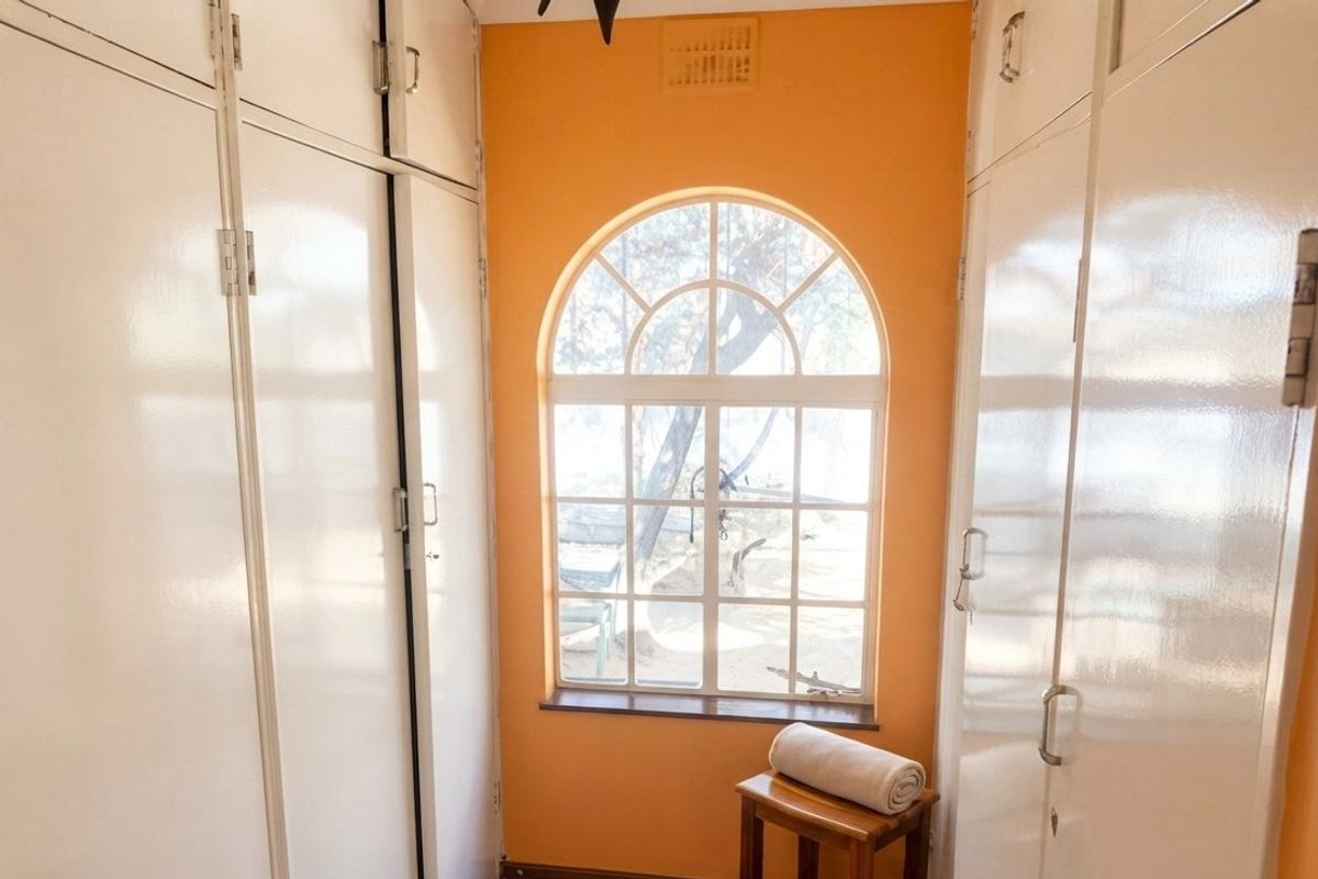 A bedroom featuring extensive built-in storage cupboards and a distinctive arched window, providing natural light and a view of the exterior.