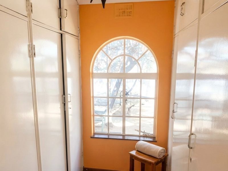 A bedroom featuring extensive built-in storage cupboards and a distinctive arched window, providing natural light and a view of the exterior.