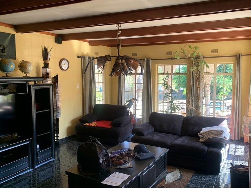 Spacious living room featuring exposed timber ceiling beams, dark tiled flooring, and large arched windows providing natural light and garden views.