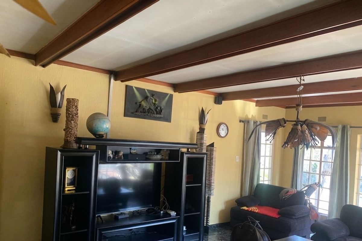 A living room featuring exposed timber ceiling beams, tiled flooring, and large windows that provide natural light.