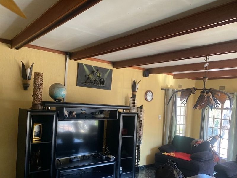 A living room featuring exposed timber ceiling beams, tiled flooring, and large windows that provide natural light.