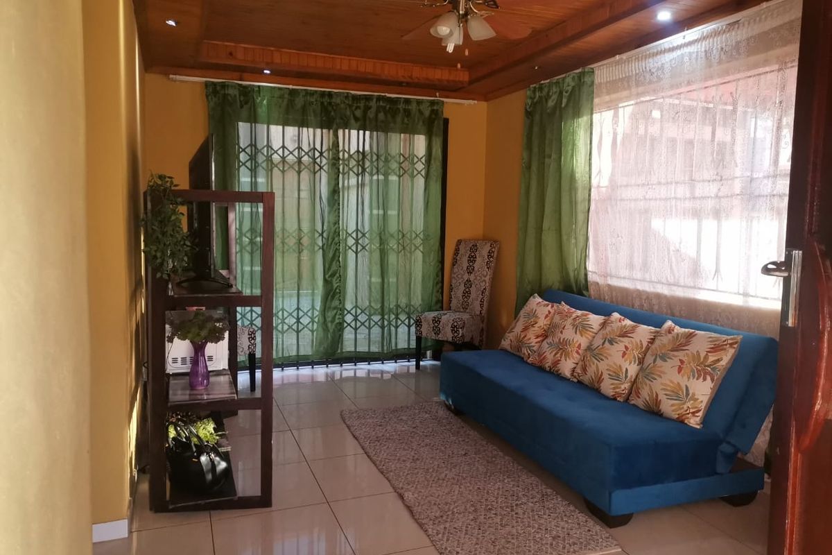 A living room featuring tiled flooring, a timber-paneled ceiling with a central fan, and a sliding glass door with an integrated security gate.