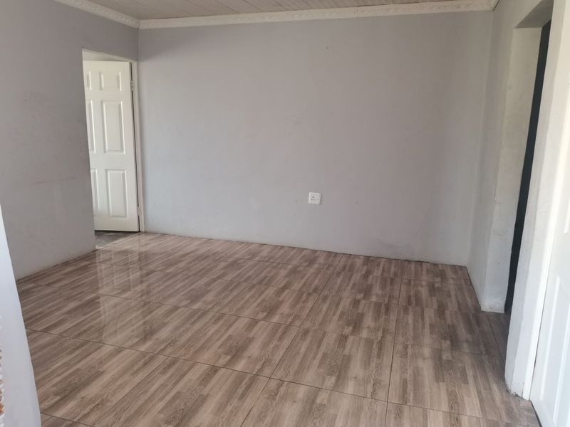 An empty living room featuring wood-look tiled flooring, neutral grey walls, and coved ceiling cornicing, providing a clean and versatile blank canvas.