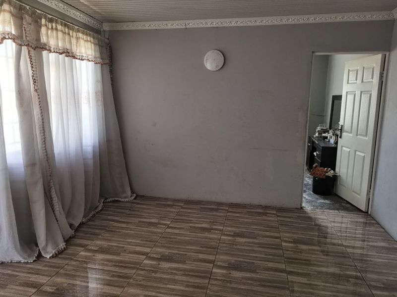 An empty living room featuring tiled flooring and decorative ceiling cornicing, requiring minor cosmetic updates to the wall finishes.