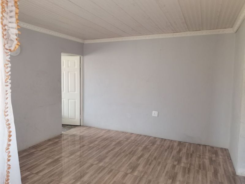 An empty living room featuring wood-look tiled flooring, a tongue and groove ceiling with decorative molding, and a neutral grey wall finish.