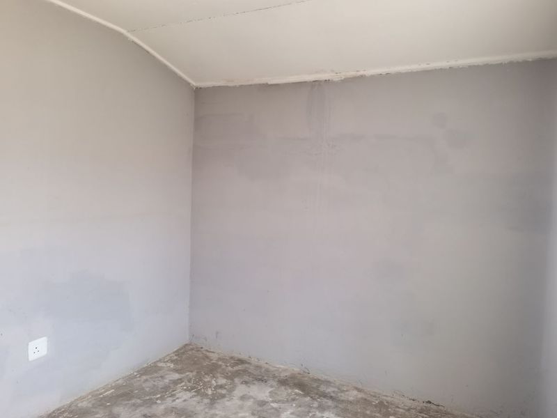 An empty, unfinished bedroom space featuring grey painted walls and a raw concrete floor, ready for final flooring and decorative finishes.