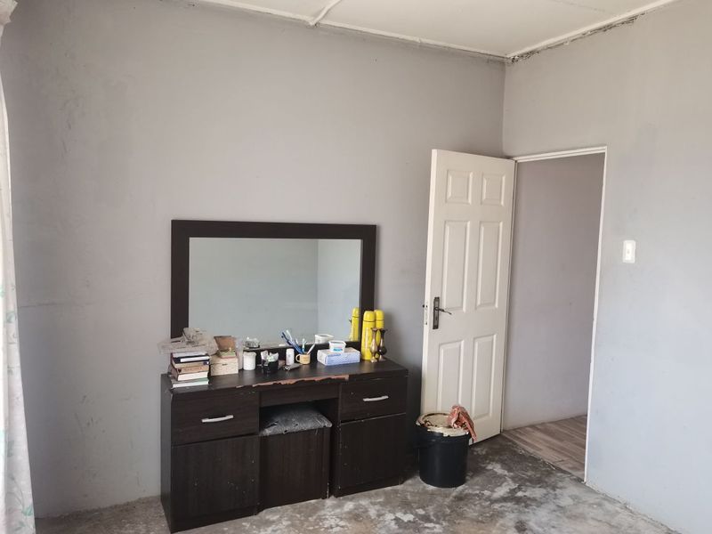 A bedroom featuring grey painted walls, a standard panel door, and unfinished concrete flooring, requiring cosmetic updates to improve the overall finish.