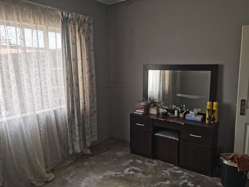 A bedroom featuring a window with curtains and exposed flooring, requiring cosmetic updates to improve the overall condition and appeal of the space.