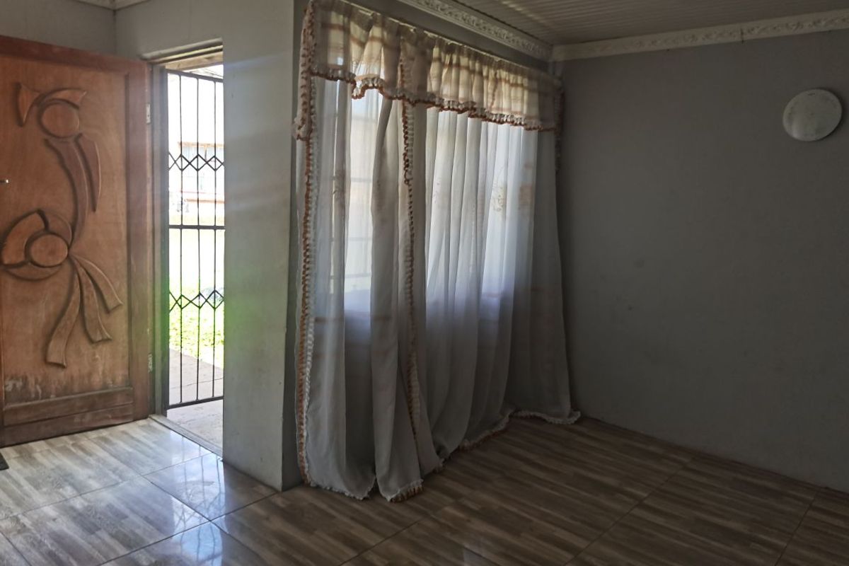 An empty living room featuring tiled flooring, a wooden entrance door, and a security gate, offering a blank canvas for interior design.