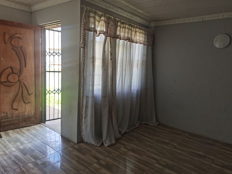 An empty living room featuring tiled flooring, a wooden entrance door, and a security gate, offering a blank canvas for interior design.