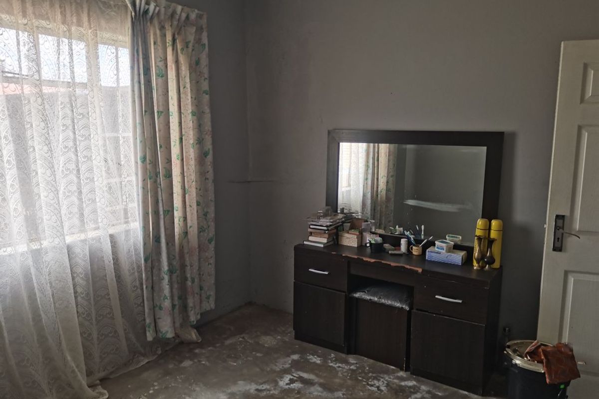 A bedroom featuring a window with curtains and a door, currently requiring significant flooring and wall finish updates to improve its overall condition.