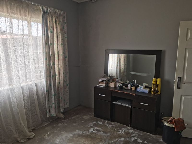 A bedroom featuring a window with curtains and a door, currently requiring significant flooring and wall finish updates to improve its overall condition.