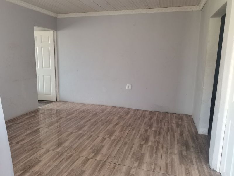 An empty living room featuring wood-look tiled flooring, neutral grey walls, and a coved ceiling, providing a blank canvas for interior design.