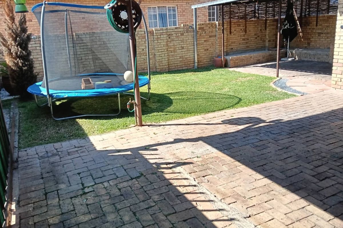A private rear courtyard featuring brick paving, a small lawn area, and a covered patio space enclosed by brick boundary walls.