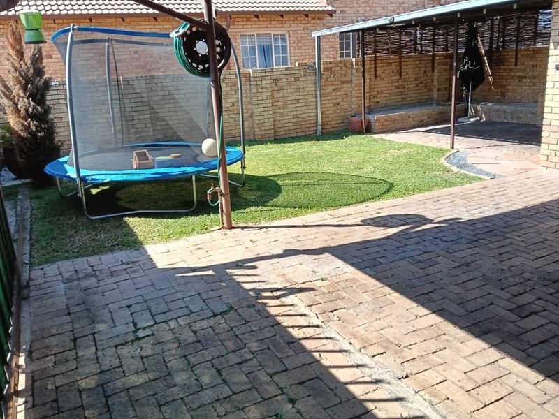 A private rear courtyard featuring brick paving, a small lawn area, and a covered patio space enclosed by brick boundary walls.
