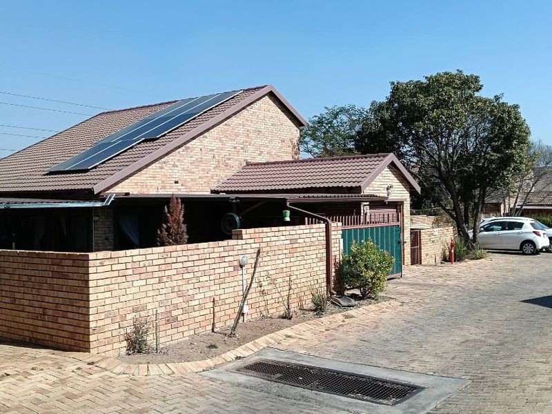 Front exterior view of a brick townhouse featuring a tiled roof, installed solar panels, and a paved driveway with a secure boundary wall.