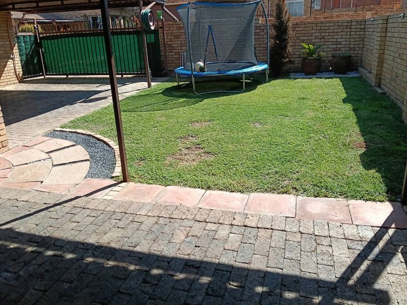A rear garden area featuring a paved patio, a small lawn, and brick boundary walls.
