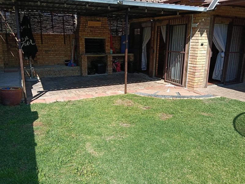 Covered outdoor patio area featuring a built-in brick braai, paved flooring, and direct access to the garden through security gates.