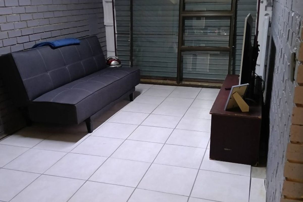 A living area featuring exposed brick walls, ceramic floor tiles, and a sliding glass door with an integrated roller shutter.