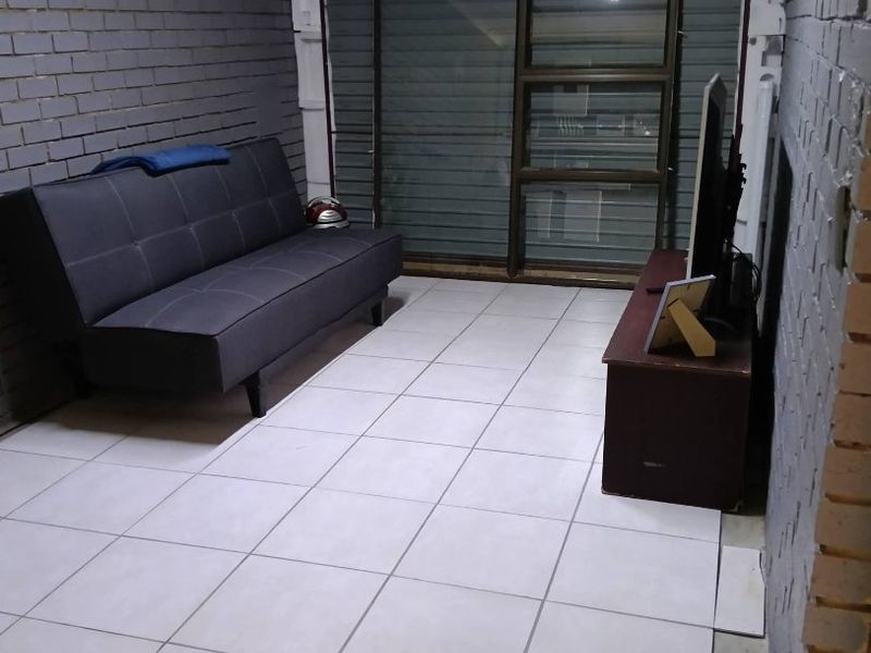 A living area featuring exposed brick walls, ceramic floor tiles, and a sliding glass door with an integrated roller shutter.