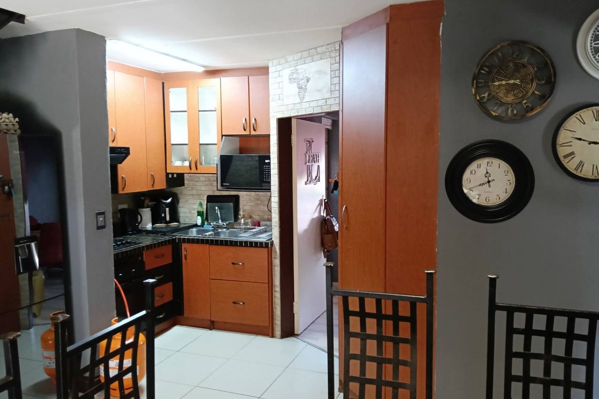 A functional kitchen featuring wood-finish cabinetry, tiled flooring, and built-in appliances, offering a practical layout with direct access to an adjacent utility area.