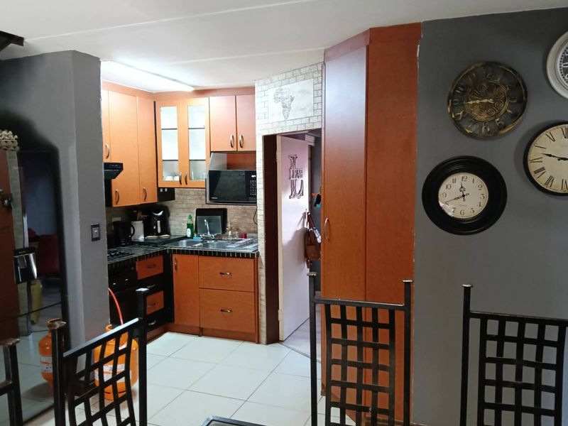 A functional kitchen featuring wood-finish cabinetry, tiled flooring, and built-in appliances, offering a practical layout with direct access to an adjacent utility area.