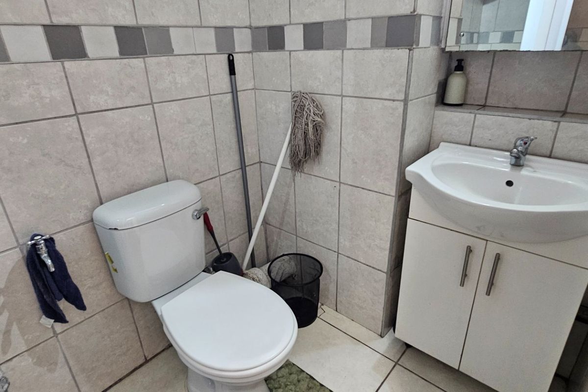 A functional bathroom featuring a white toilet, vanity cabinet with integrated washbasin, and neutral wall tiling.