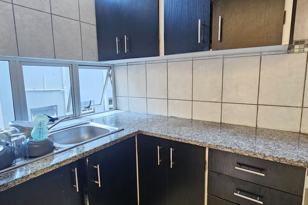 A functional kitchen featuring dark cabinetry, granite countertops, a stainless steel sink, and tiled backsplash with natural light from the window.