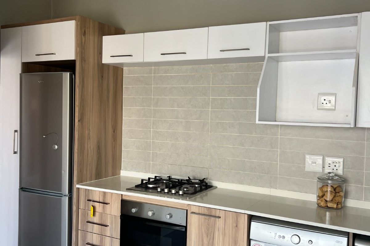 Modern kitchen featuring wood-tone and white cabinetry, stone countertops, a gas hob, built-in oven, and tiled backsplash with integrated appliance spaces.