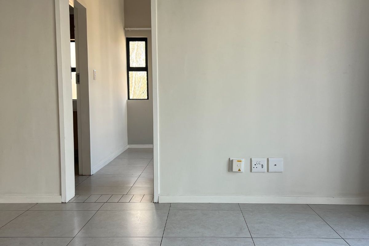 An empty living area featuring neutral tiled flooring, clean walls, and a doorway leading to an adjacent hallway.