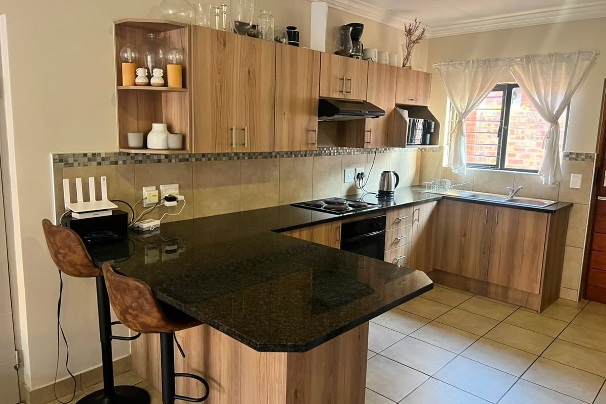 A functional kitchen featuring wood-finish cabinetry, dark granite countertops, a breakfast nook, and tiled flooring with a tiled backsplash.