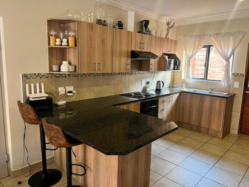 A functional kitchen featuring wood-finish cabinetry, dark granite countertops, a breakfast nook, and tiled flooring with a tiled backsplash.