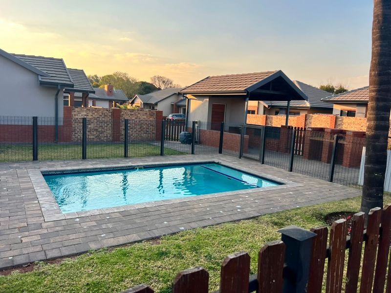 Outdoor pool area featuring a rectangular swimming pool, paved surround, and a covered patio structure within a fenced garden setting.