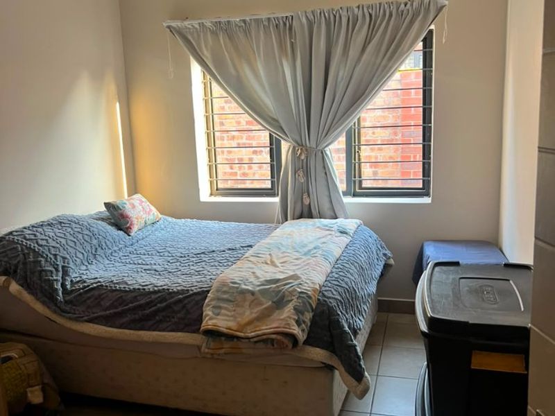 A functional bedroom featuring tiled flooring, coving, and a window fitted with security bars, providing a neutral space for rest.