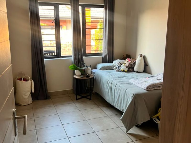 A functional bedroom featuring tiled flooring and aluminium-framed windows with security bars, offering a neutral base for interior design.