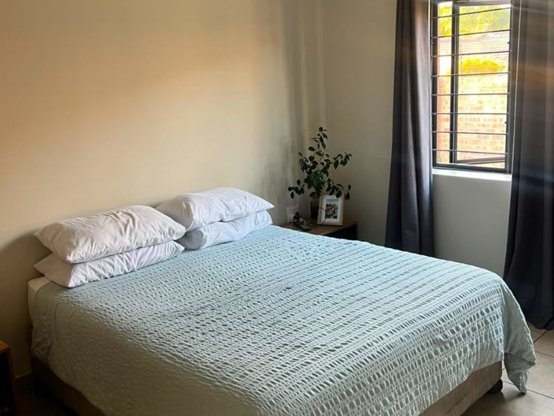 A functional bedroom featuring tiled flooring, security bars on the window, and neutral wall finishes.