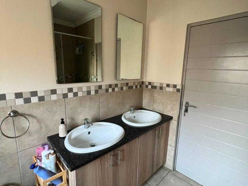A functional bathroom featuring a double vanity with granite countertops, tiled backsplash, and dual wall-mounted mirrors.