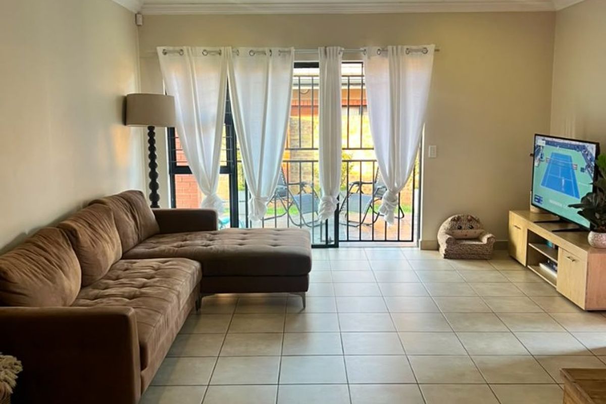 A spacious living room featuring neutral tiled flooring, recessed downlighting, and a sliding glass door providing access to an outdoor area with security gate.