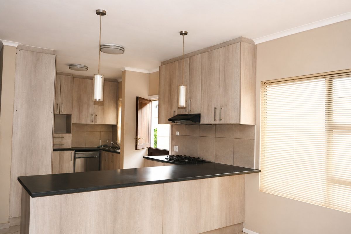 Modern kitchen featuring light wood-grain cabinetry, dark laminate countertops, a gas hob with extractor fan, and integrated dishwasher, finished with neutral tiled backsplash.