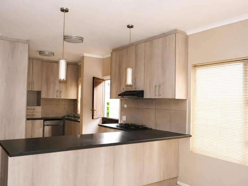 Modern kitchen featuring light wood-grain cabinetry, dark laminate countertops, a gas hob with extractor fan, and integrated dishwasher, finished with neutral tiled backsplash.