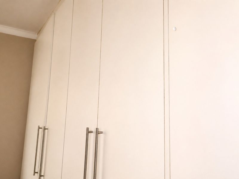 A close-up view of neutral-toned built-in bedroom cupboards featuring modern stainless steel handles.