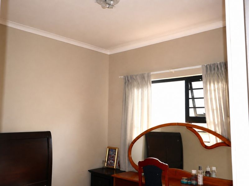 A bedroom featuring neutral wall finishes, coving, and an aluminium-framed louvre window providing natural light.