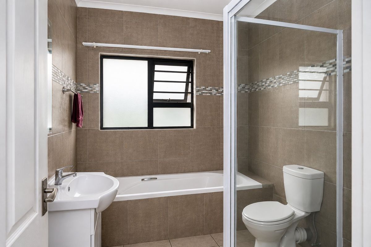 A clean, functional bathroom featuring a built-in bathtub, separate shower enclosure, vanity basin, and toilet with neutral wall and floor tiling.
