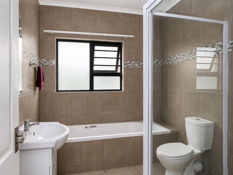 A clean, functional bathroom featuring a built-in bathtub, separate shower enclosure, vanity basin, and toilet with neutral wall and floor tiling.