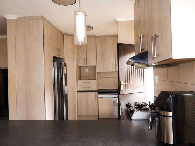 A functional kitchen featuring light wood-tone cabinetry, dark stone countertops, a gas hob with extractor fan, and integrated dishwasher.