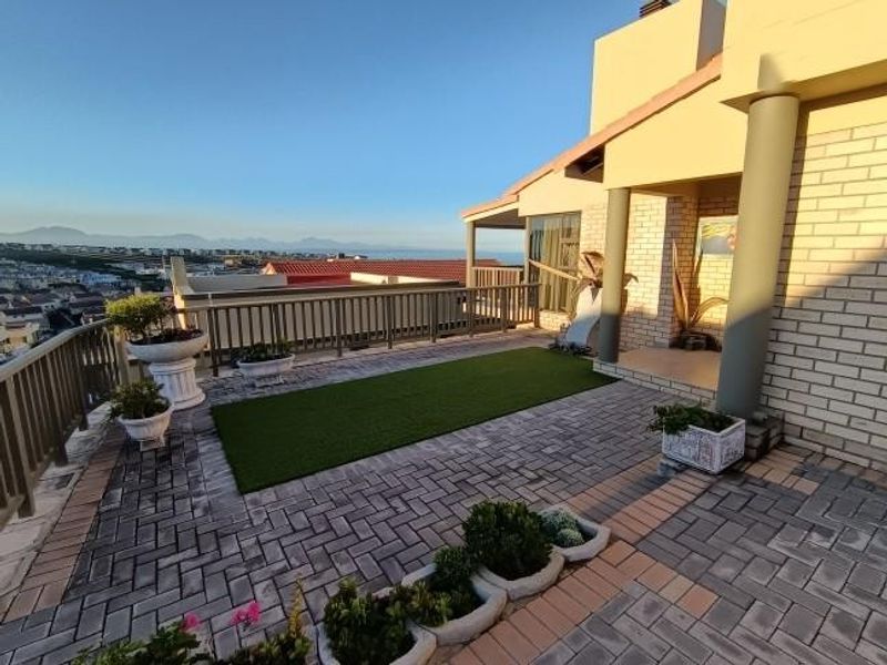 An elevated outdoor patio area featuring paved flooring, structural columns, and a railing, offering expansive views of the surrounding landscape.